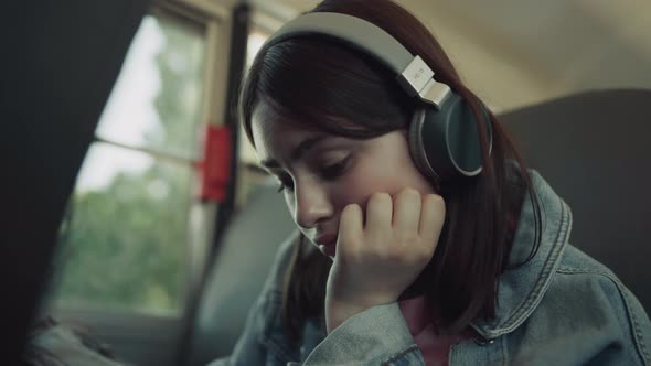 Closeup Upset Girl Sitting Schoolbus Alone with Headphones Waiting for Ride