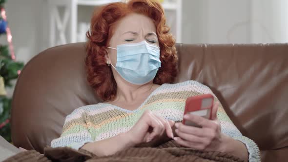 Portrait of Isolated Caucasian Woman in Covid Face Mask Using Smartphone and Sneezing at Home on New