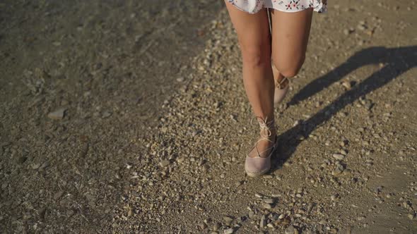 The Girl Walks on the Beach with Pebbles in Shoes.