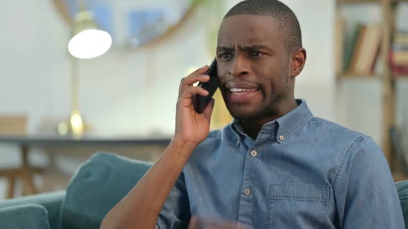 Young African Man Angry on Smartphone on Sofa