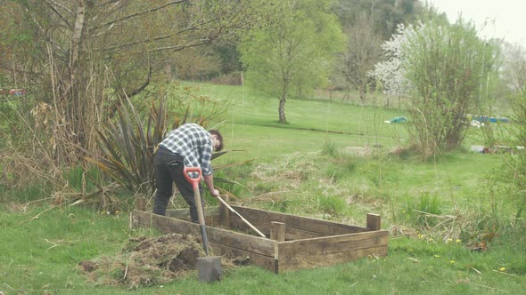 Young gardener scraping off topsoil for raised garden bed WIDE SHOT