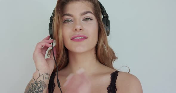 Attractive Woman Puts Headphones Over Ears Light Flirting and Posing at Camera