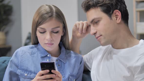 Talking Young Couple Using Smartphone and Disussing Online Product