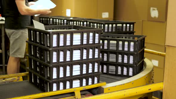 Black crates filled with music vinyl records on a conveyor and checked by worker