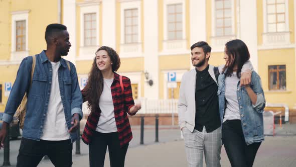 Friends Tourists in Casual Clothes Are Walking in City with Backpacks Talking and Laughing on Summer