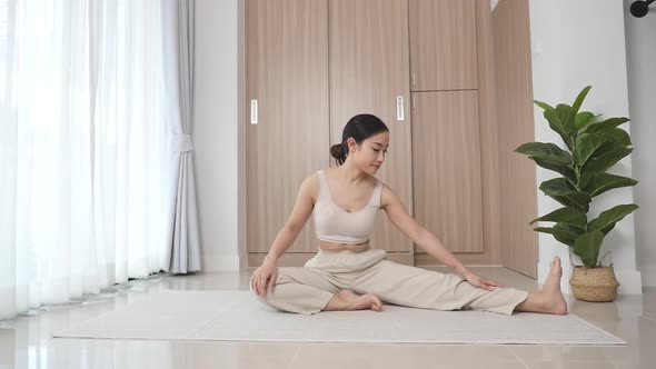 An athletic woman sits on the floor by a large window during her morning yoga 