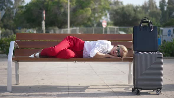 Exhausted Tired Caucasian Businesswoman Falling Asleep on Bench in City with Luggage