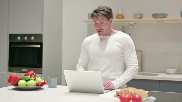 Middle Aged Man Doing Video Call on Laptop in Kitchen