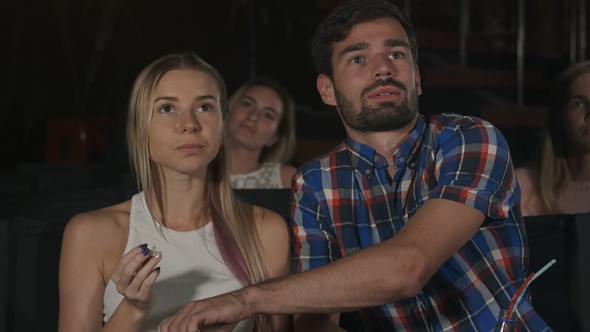 Happy couple sitting in movie theater, eating popcorn, smiling