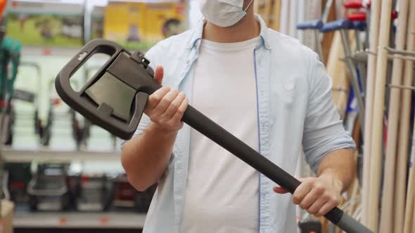 Man in a Medical Mask Picks Up an Axe in the Construction Department of a Shopping Center