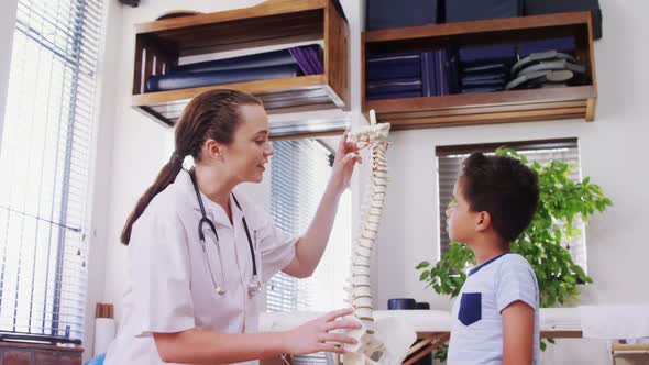 Female physiotherapist explaining spine model to boy patient