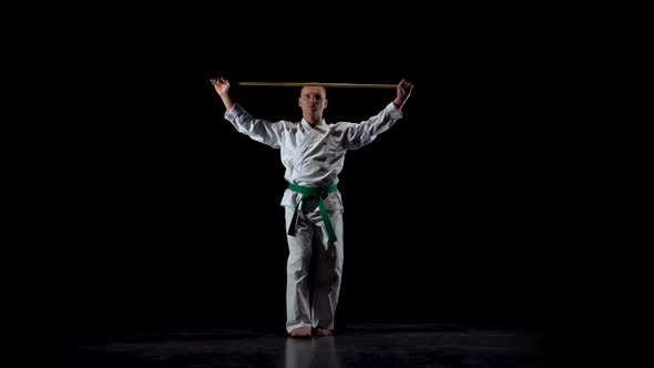 Kendo Fighter on White Kimono Practicing Martial Art with the Bamboo Bokken on Black Background