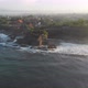 Aerial pan view of waves crashing against a temple with mountain views in the distance - VideoHive Item for Sale