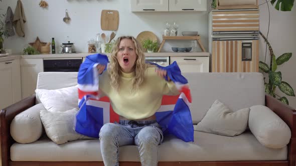 A Woman Fan of the Icelandic National Team with the Flag of Iceland Watches TV at Home