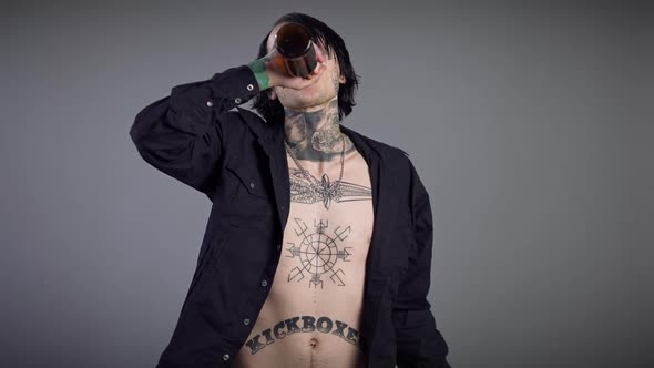 Tattooed Young Man with Unbuttoned Shirt Drinking Beer From Bottle Smiling Looking at Camera