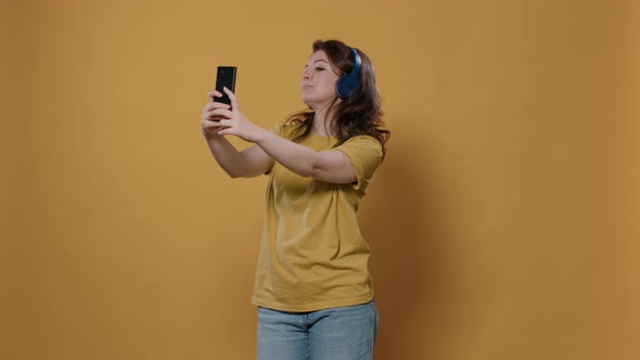 Casual Woman Taking a Selfie Using Mobile Phone While Listening to Music on Wireless Headphones