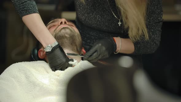 Blondie Woman Barber Cutting Beard Hair on Her Client with Straight Razor