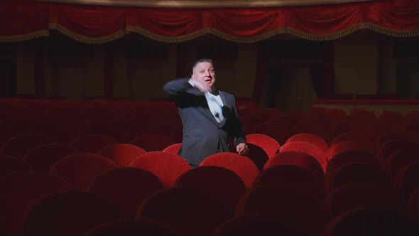 Man in empty theater. Rich man in suit taking off facial mask and says something among rows