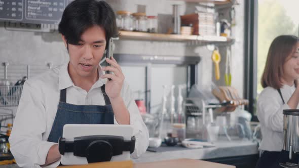 barista man coffee maker receive phone call and record pre order to computer in coffee cafe shop