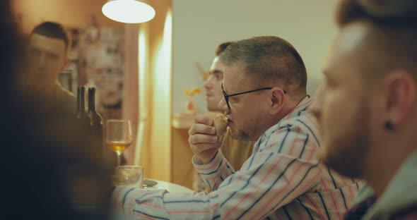 Adult Man with Glasses Eats Pizza Among Friends