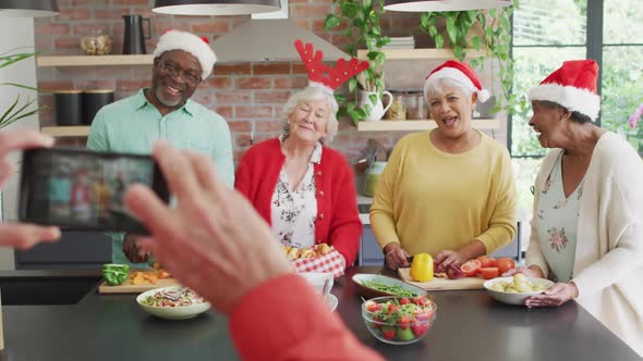 Group of happy diverse senior friends cooking together and taking selfie at christmas time