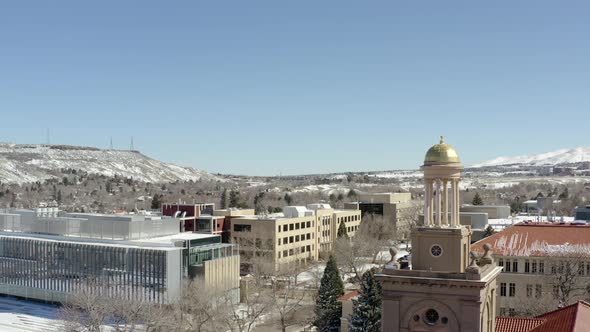 An aerial orbiting shot of a small tower in the middle of a small town overlooking snowy mountains.