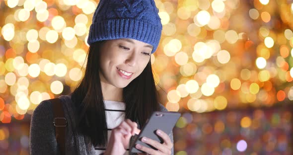 Woman look at mobile phone over christmas light decoration