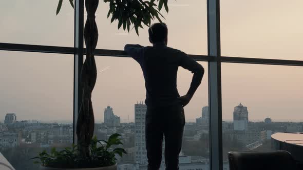 Silhouette Businessman Stands Near Tall Window In Office. Man Stand Near Window On Evening City.