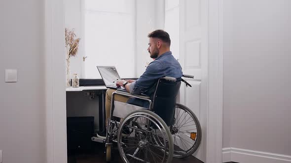Man in Wheelchair Working on Laptop Near Window at Home