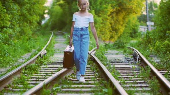 Girl Holding Vintage Suitcase and Walking on Railroad Tracks