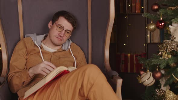 Man Reading Book Near Christmas Tree