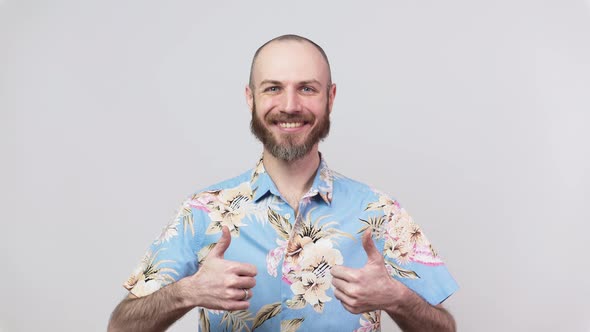 Happy bearded man wearing hawaiian shirt showing thumbs up over white background.