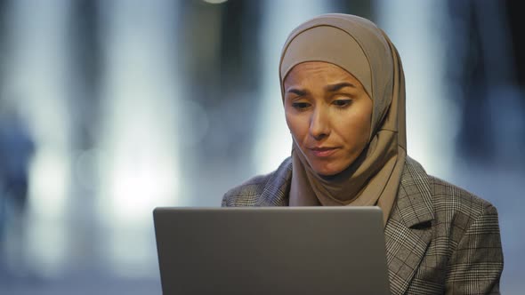 Portrait of Muslim Business Woman User in Hijab Sits in Evening City Outdoors Working with Laptop