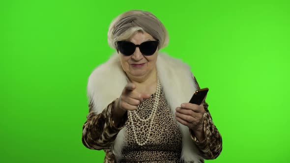 Caucasian Grandmother Woman Using Smartphone, Pointing at Camera with Hand