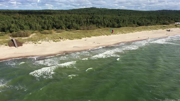 AERIAL: Surfer with Kite Visible in the Forest and Sandy Beach Background