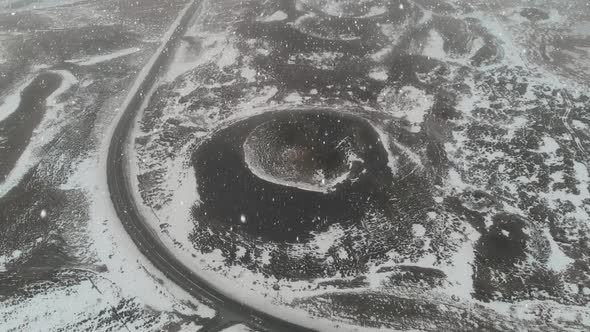 Aerial view of snow falling on volcanic crater and frozen lake at Icelandic high lands, pull back dr