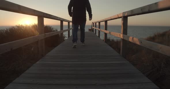 Man walks over a wooden pathway towards the sunset on Sylt