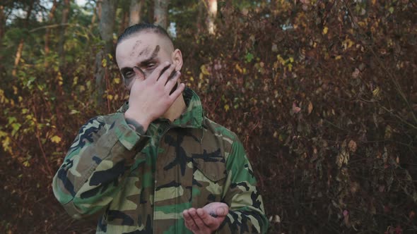 Brave Soldier in Camouflage Smears Soot Strips on Face at a Forest Before Fight