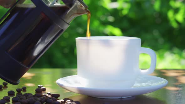 Pouring Coffee Into Cup on the Table in the Garden Scenery