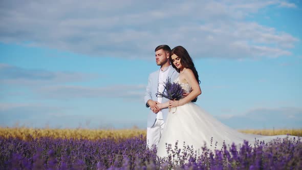 Newlyweds in Love are Walking Through a Field of Lavender Flowers