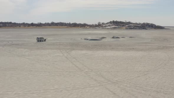 White SUV Safari Vehicle Driving In Makgadikgadi Salt Pan Towards Kubu Island In Botswana. - Aerial