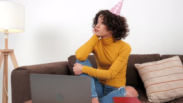 Upset Curly Woman in Party Hat Looking Away Celebration Birthday Alone at Home