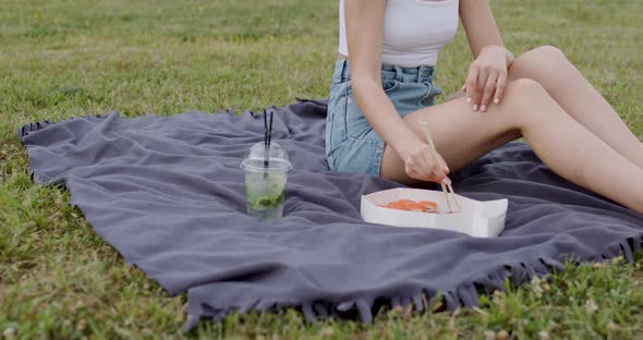 One Summer Evening at a Picnic a Young Woman Eats Sushi Rolls of Various Kinds and Drinks a Cold