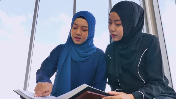 Two Muslim Asian women wearing traditional hijab are reciting prayers in the Quran.