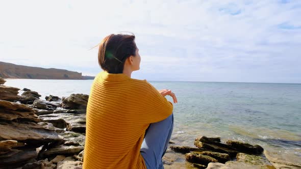 Young Woman Sitting on Sea Shore and Looking Into the Distance