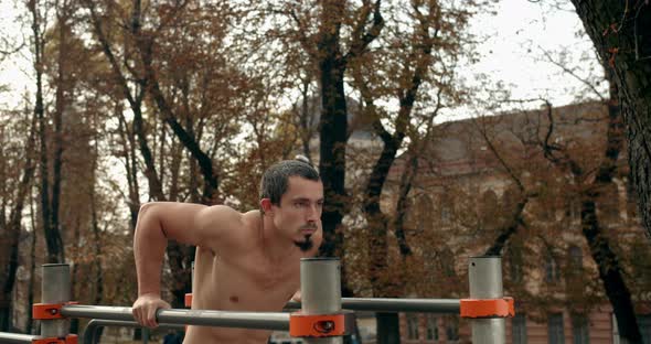 Young Man Is Doing Push Ups on Uneven Bars on Outside 