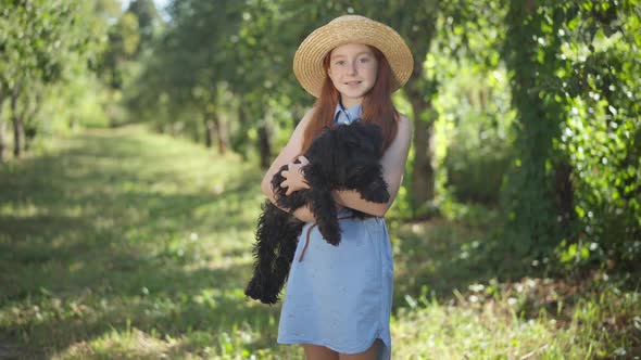 Happy Teenage Girl Posing with Black Norfolk Terrier in Summer Spring Park on Sunny Day