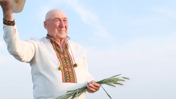 Happy Grandfather Farmer Holding an Ear of Wheat Against a Blue Sky