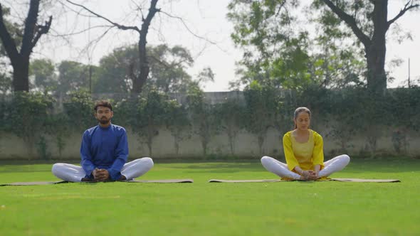 Butterfly Yoga pose or Titliasana is being done by an Indian couple in an Indian outfit