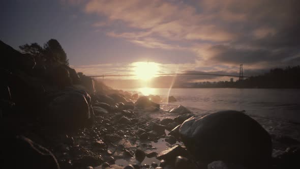 Warm hazy sunrise on rocky beach with bridge